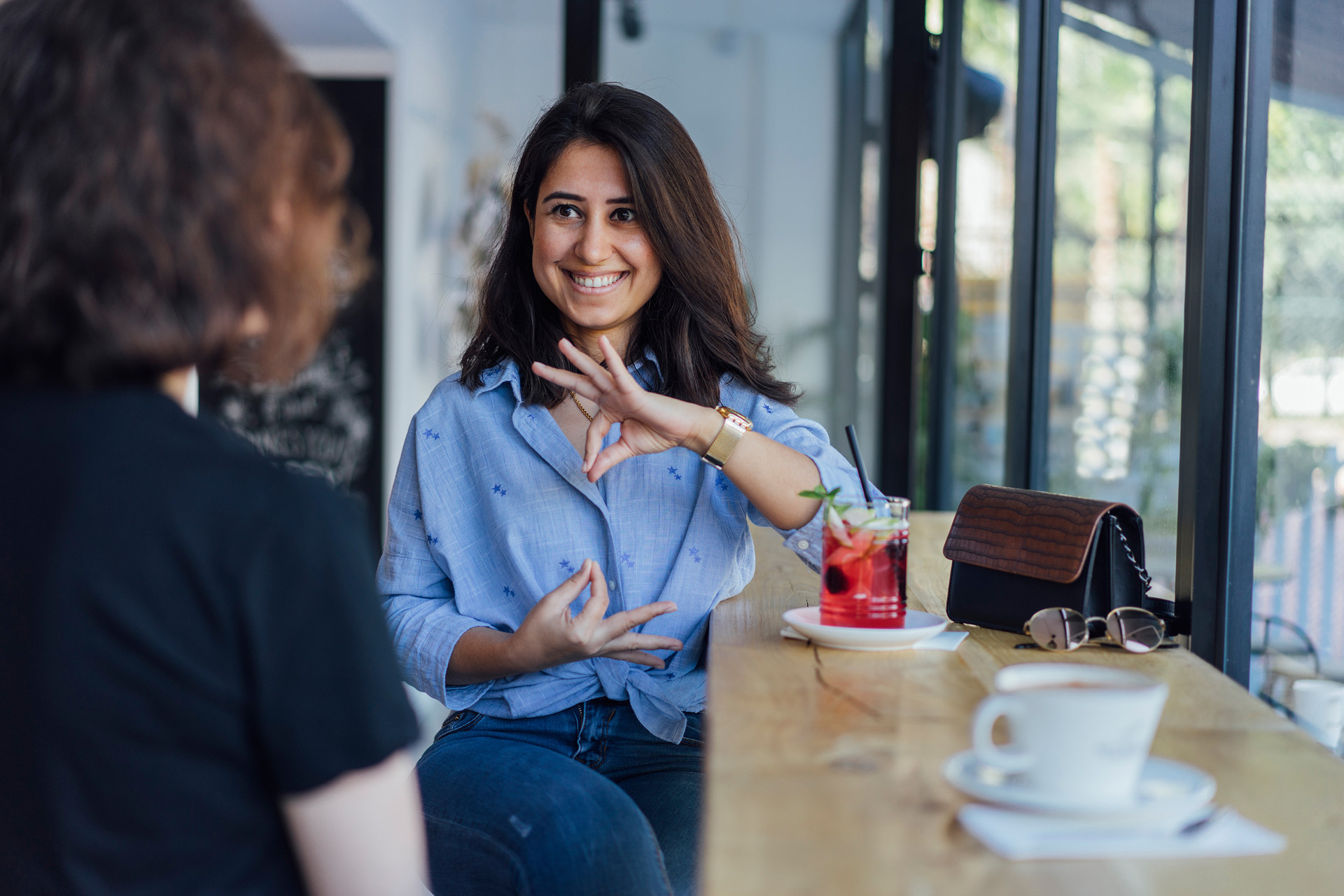 Eine Frau sitzt an einem Tisch in einem Café und unterhält sich mit jemandem.