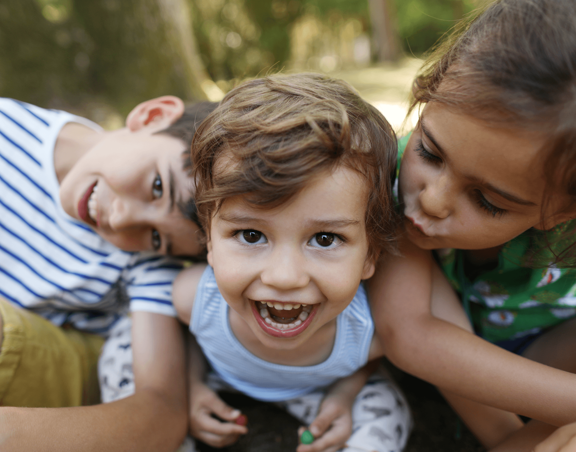 Drei Kinder liegen auf dem Boden in einem Park, lachen und spielen.